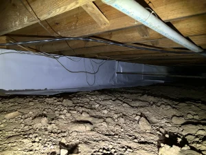 Crawl space before encapsulation, showing exposed soil and pipes.