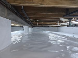 Clean, encapsulated crawl space with white plastic lining covering the floor and walls. Exposed wooden beams and plumbing pipes run along the ceiling.